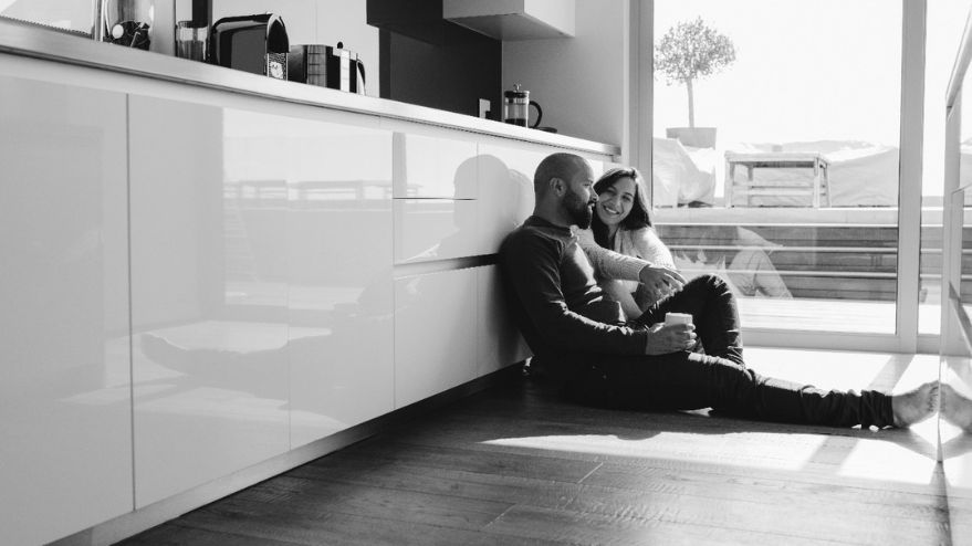 Couple sitting down next to each other in a kitchen planning smiling
