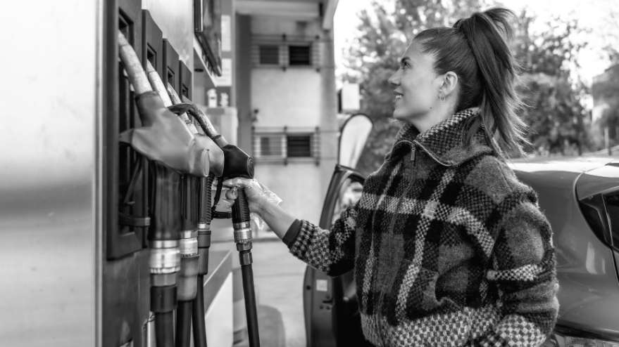 A lady holding a pump at a filling station about to put fuel in their car
