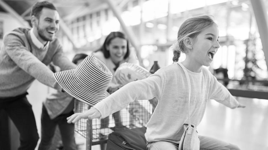 Family pushing young girl sat on a luggage trolley